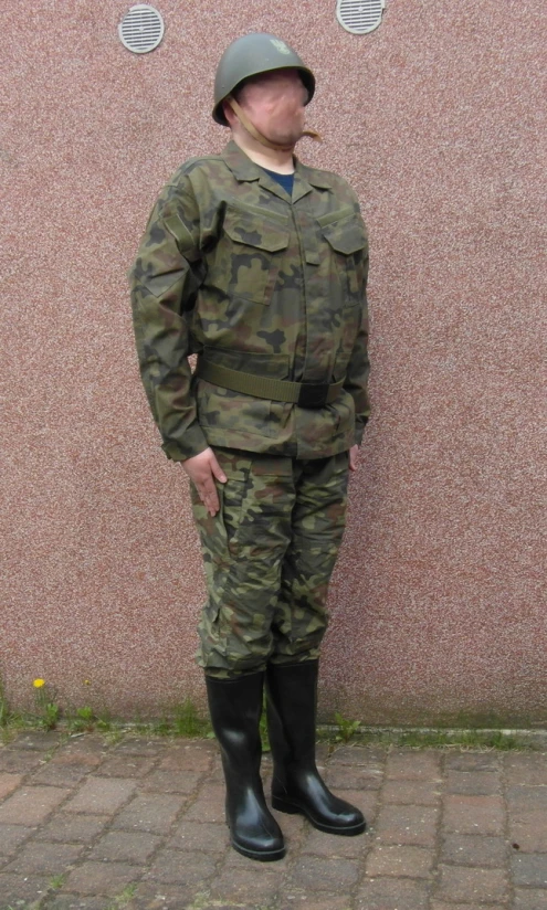 the soldier is posing against the wall in the military uniform