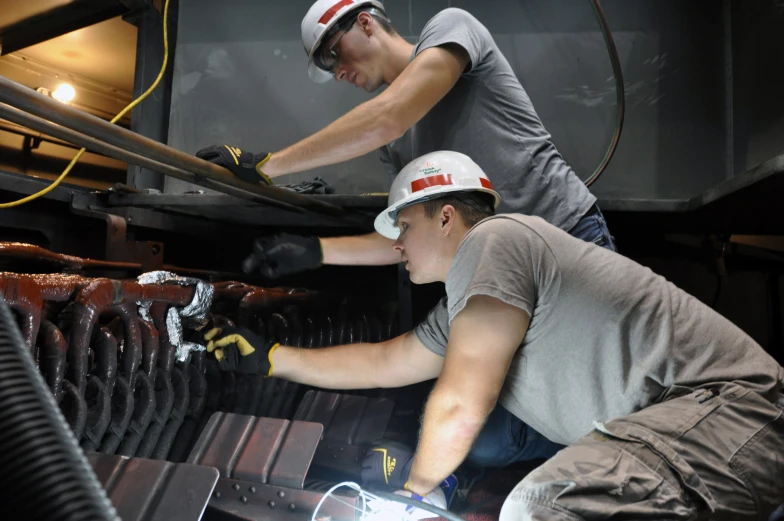 two men in front of a machine working on a metal item