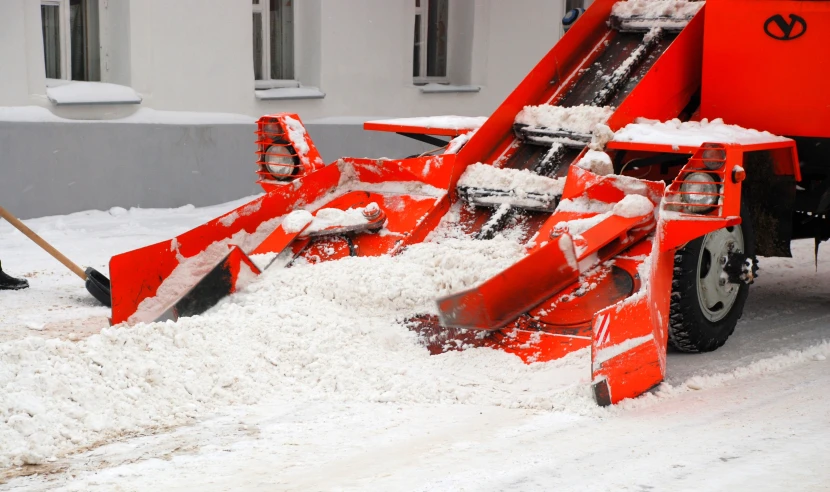 a red snow plow is moving snow on the street