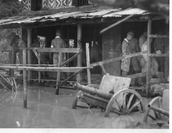 black and white pograph of men standing outside of a shack