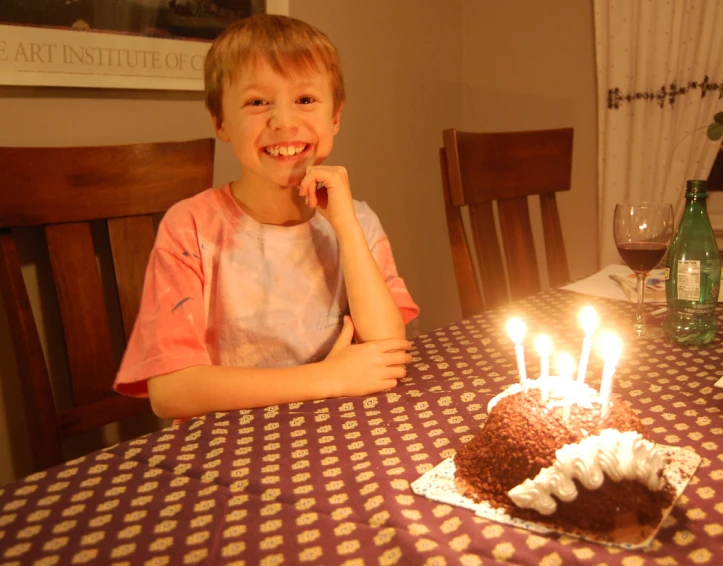 the child sits at the table with a cake in front of him