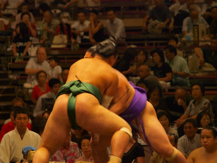 two sumo women perform stunts while people watch from the stands