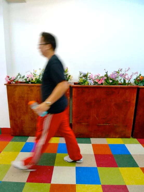 a man walking across the floor in front of plants