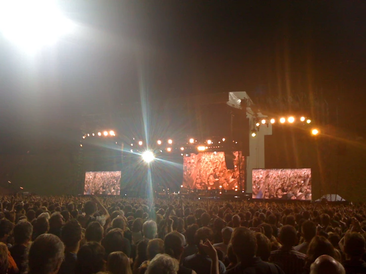 a large crowd watches an electronic display on a stage