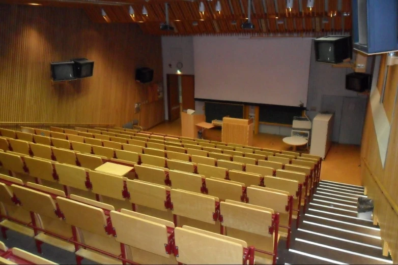 a lecture hall with red chairs and two speakers