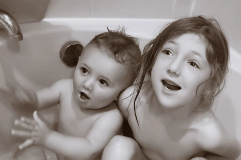 two babies sit in the bathtub with bubbles coming out of their mouths