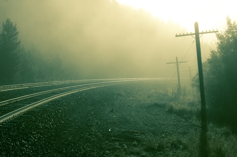 sun peeking out of fog on an empty train track