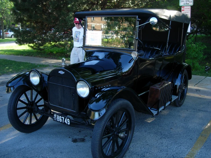 a person in white uniform stands near a vintage black car