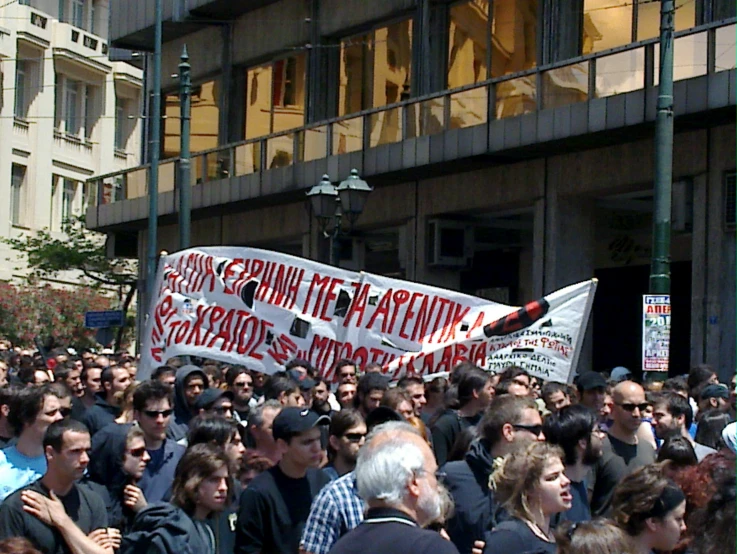 a large crowd is on a sidewalk holding signs