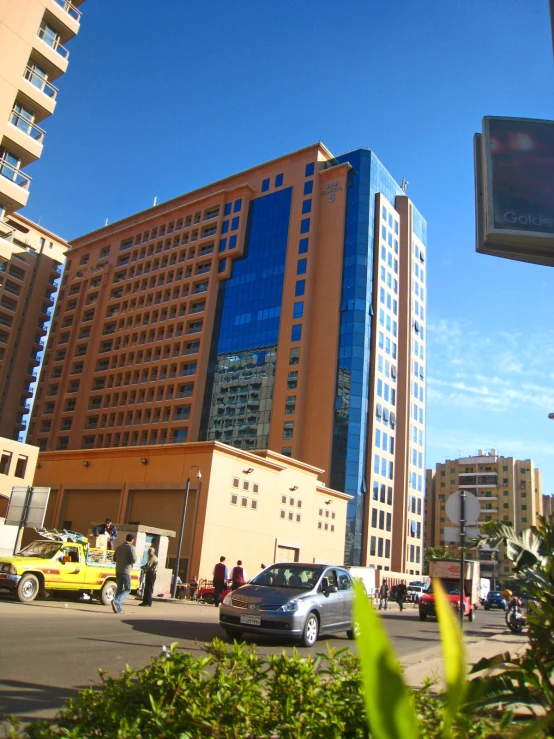 a tall brown building with blue windows and a yellow car parked in the street