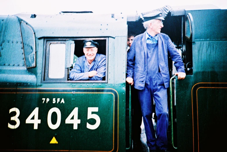 a man wearing a blue suit and hat standing outside of a green train car