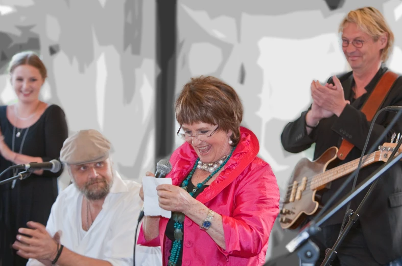 an older woman talking into a microphone while holding a card