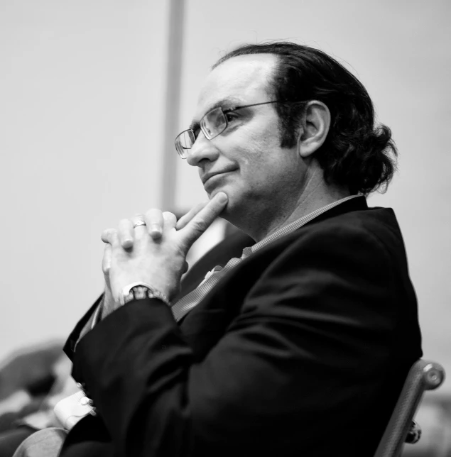 man in business attire sitting in chair during a conference