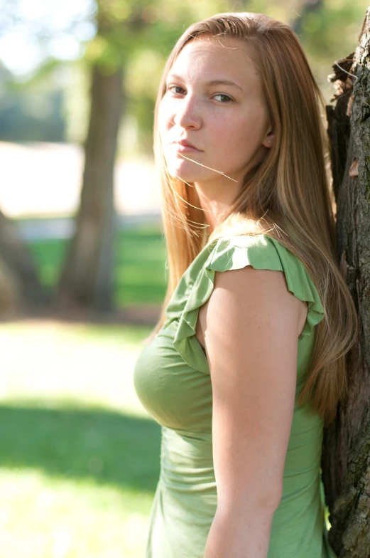 a woman leaning on a tree trunk near grass