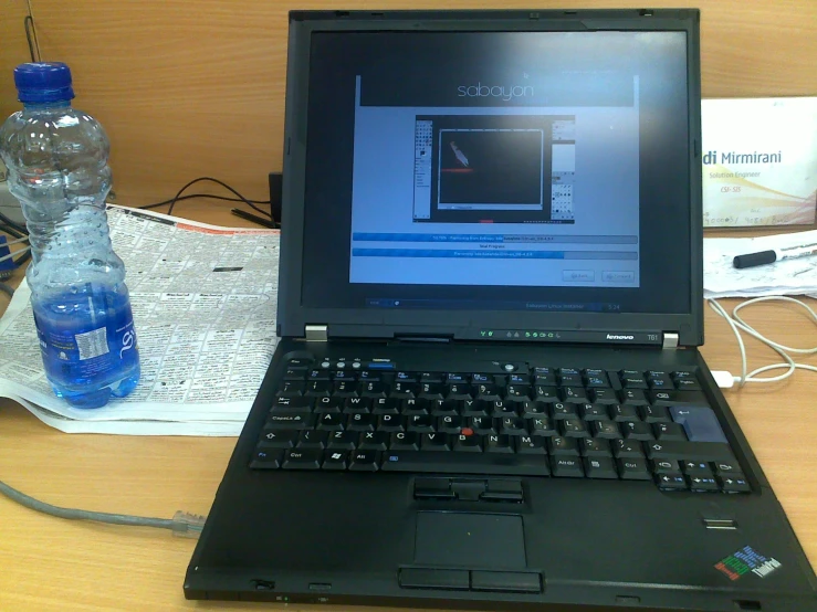 a laptop sits on a table next to a bottle