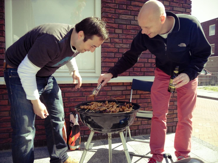 two men outside with the man cooking soing on a grill