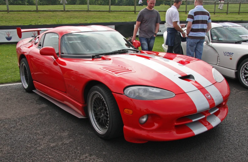 two men stand next to a red sports car