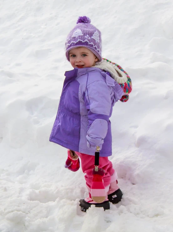 a little girl in purple coat and pink snow boots