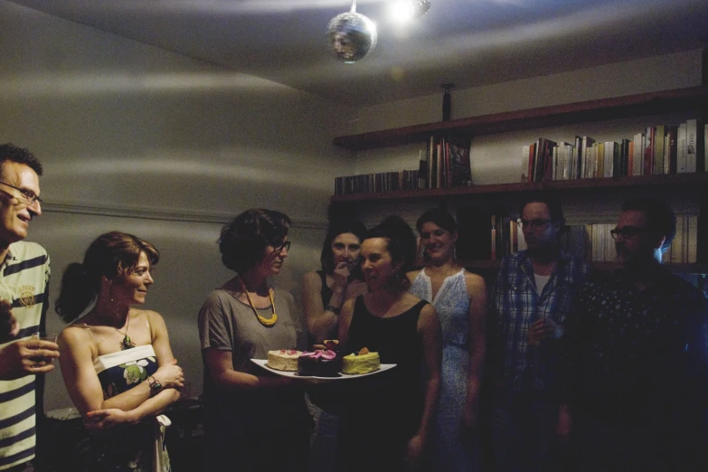 a group of people standing around talking and eating cake