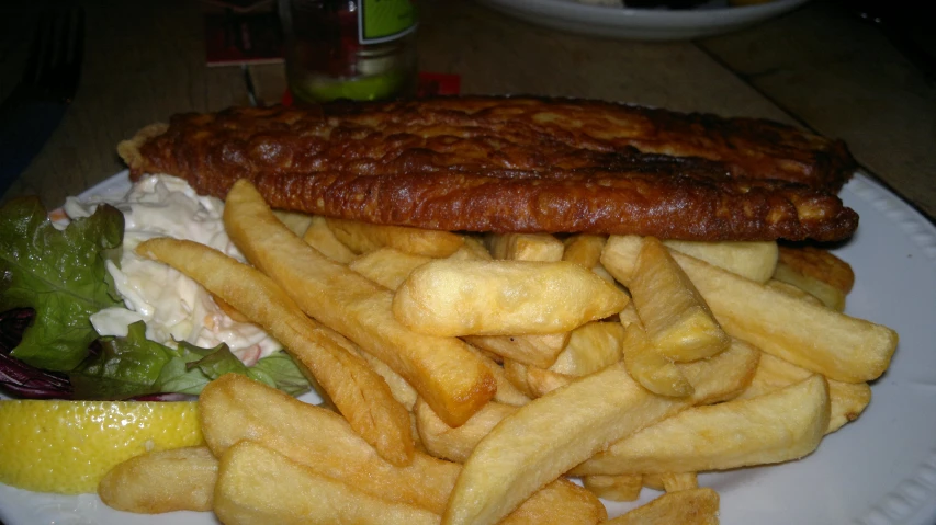 a large fish fillet sits on top of french fries