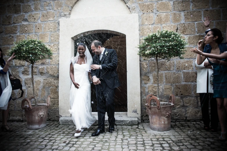 a bride and groom in the rain in front of an arch