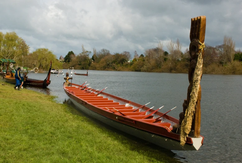 people and canoes sit on the shore by a lake