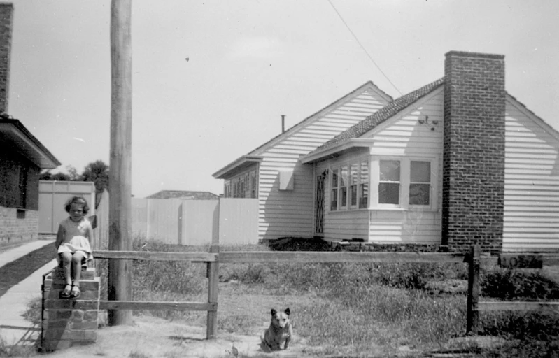 a little girl standing in front of a house and her dog