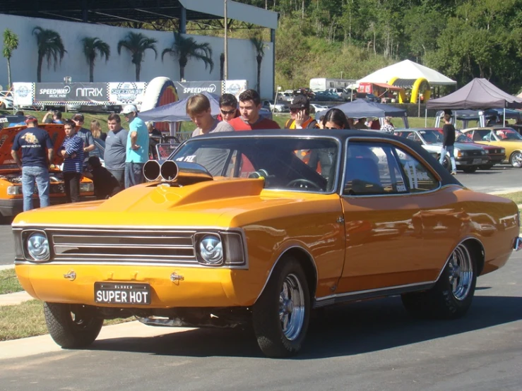 the old orange car is driving in front of the other people