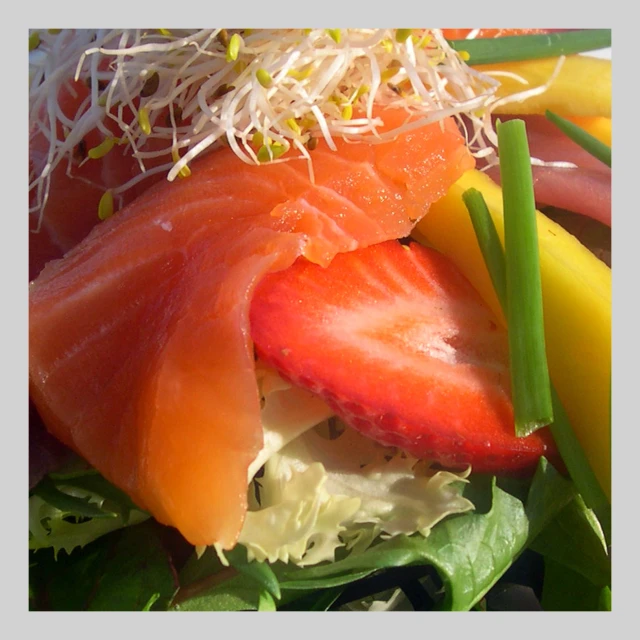 a salad with a piece of salmon, lettuce, and strawberries