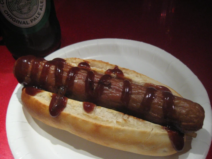 dog on white plate covered with ketchup next to a bottle of beer