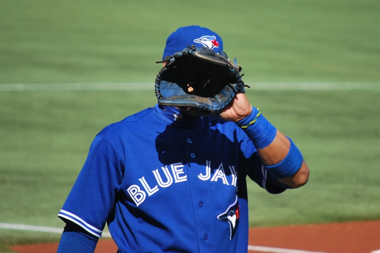 baseball player wearing blue jacket in outfield with glove covering face