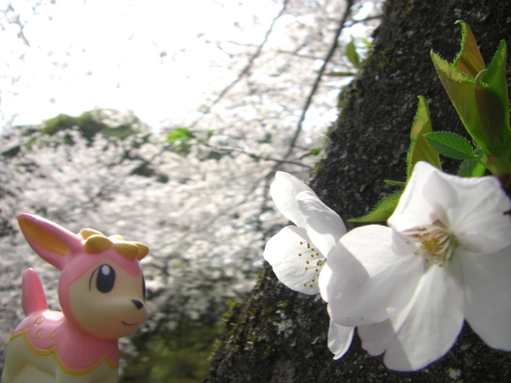 a pink toy dog standing by a tree with white flowers