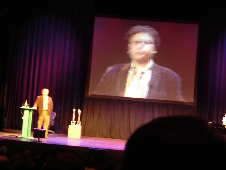 a man standing on stage in front of a crowd of people