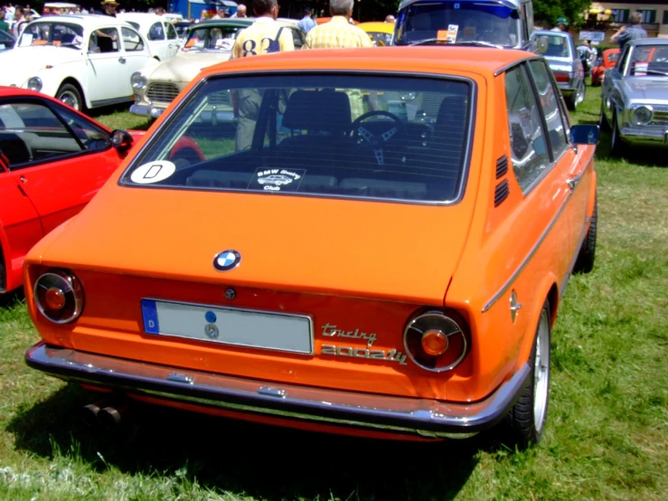 a car is shown on a grassy lot with people looking at it