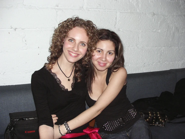 two girls are hugging on a couch in front of a brick wall