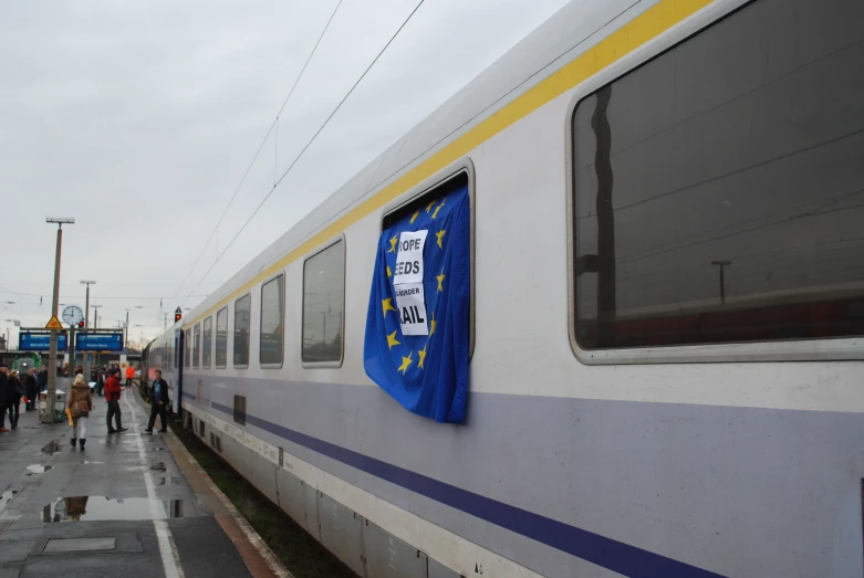 people standing outside a train car that has a european flag hanging on it