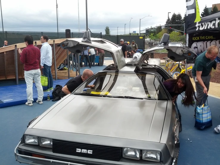 there are many people standing around an old car