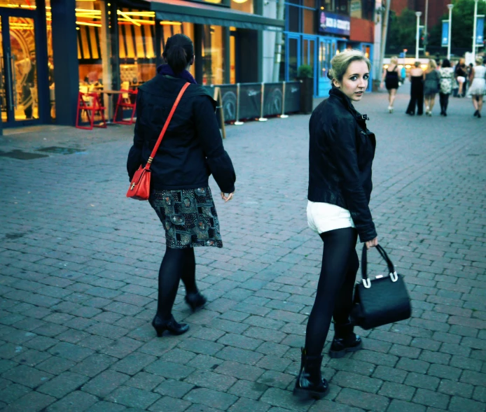 two women walking on the sidewalk carrying their bags