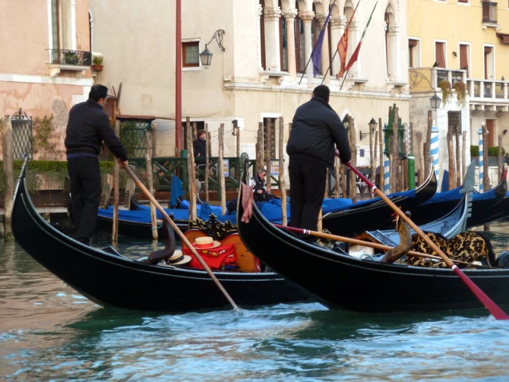 two men with large stick's on boats in a canal