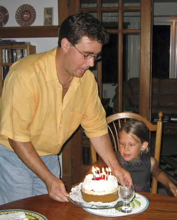 a man helping a little girl cut into a cake