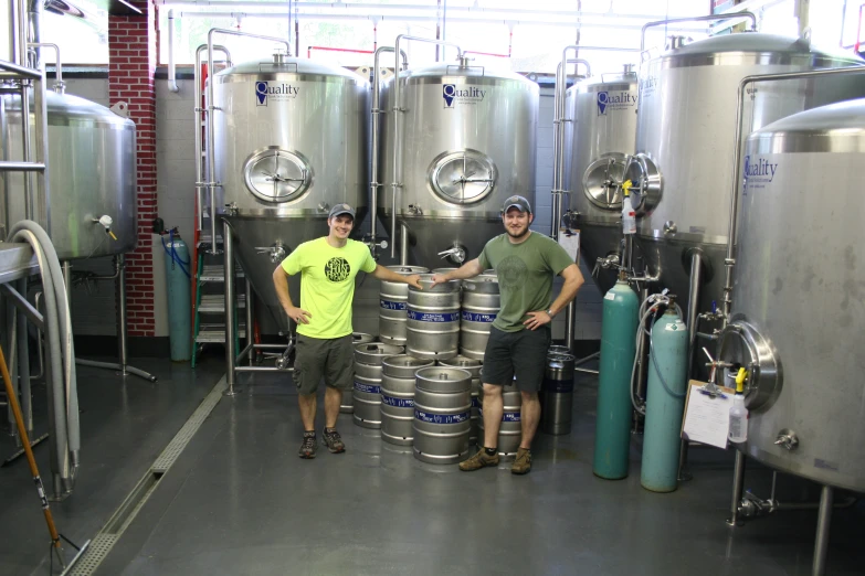 two men standing next to a pile of stainless steel kegs