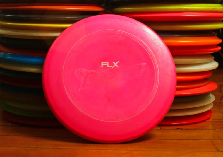 a pink frisbee sitting next to a pile of multicolored plates