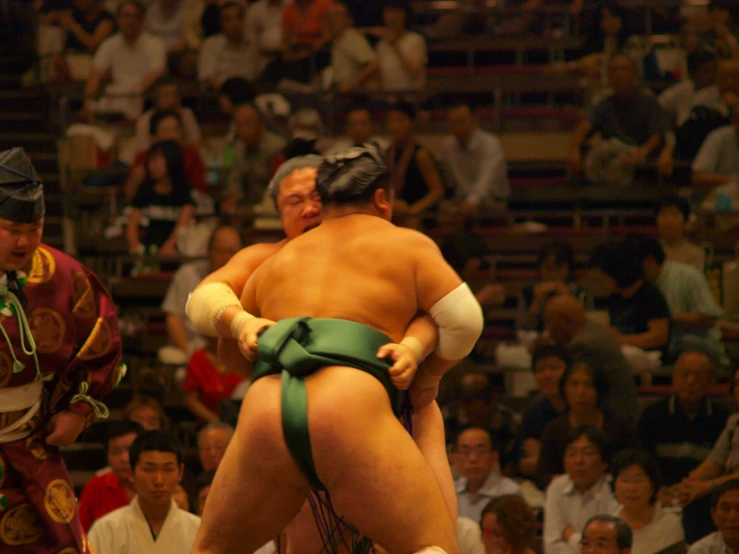 a sumo wrestler is wrestling while another wrestlers watches