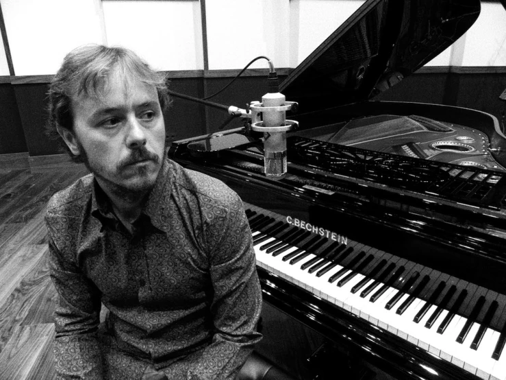 a man standing next to a piano looking at the camera