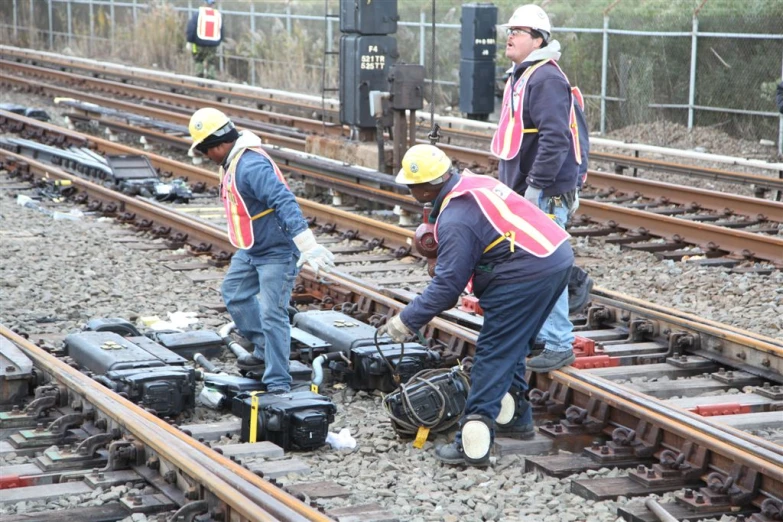 two men on train tracks fixing a broken electric box