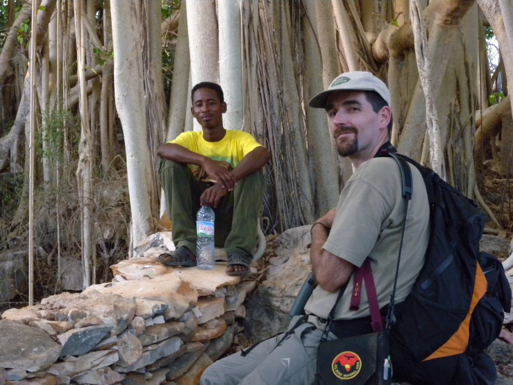 a man sitting on a tree while another man with a backpack sits in front