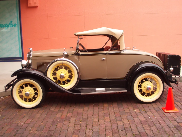an antique car with a tan top parked by a brick sidewalk