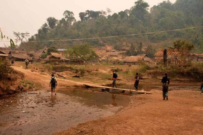 men in village walking on dirt road with water