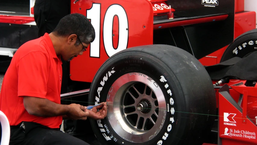 a man works on a tire that is attached to a red car