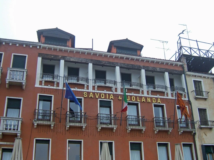 a red brick building with balcony balconies and two flagpoles